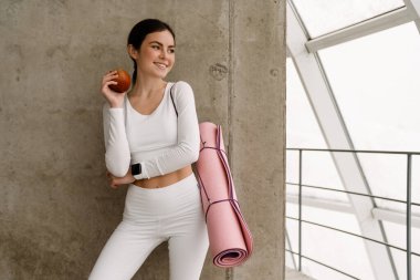 Yoga minderi tutan gülümseyen genç bir kadın.