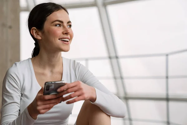 Brunette Glimlachende Vrouw Met Behulp Van Mobiele Telefoon Tijdens Yoga — Stockfoto