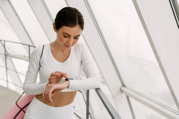 Młoda Zadowolona Kobieta Pomocą Smartwatch Stojąc Maty Jogi Wewnątrz — Zdjęcie stockowe