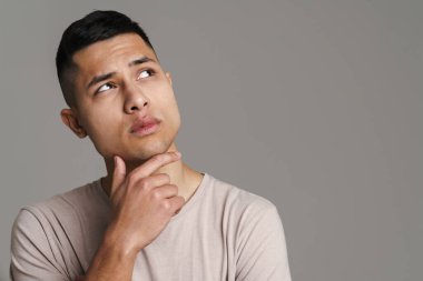 Esmer, kafası karışmış genç bir adam, gri duvarın üzerinde izole bir şekilde düşünüyor ve yukarı bakıyor.