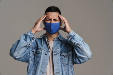 Mutsuz adam, baş ağrısı çeken, koruyucu maske takan, gri arka planda izole edilmiş.