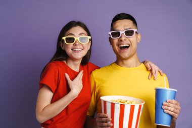 Üç boyutlu gözlüklü neşeli çift menekşe arkaplanından izlenmiş film izlerken patlamış mısır yiyorlar.