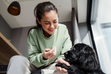 Gülümseyen esmer kadın köpeğini evde okşuyor.