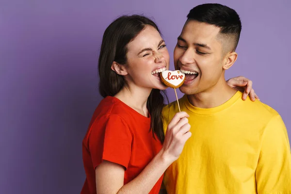 Щаслива Пара Яка Підморгує Споживаючи Печиво Відокремлене Над Фіолетовою Стіною — стокове фото