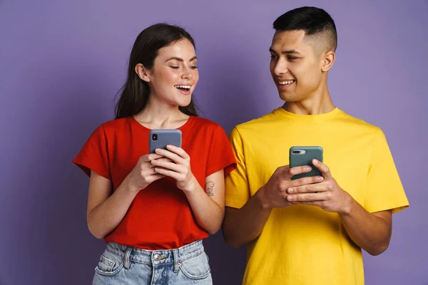 紫色の背景に隔離された携帯電話を使用している間 幸せな美しいカップル笑顔 — ストック写真