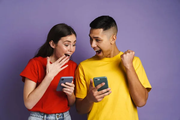 紫の背景に隔離された携帯電話を使用している間興奮したカップルは勝者のジェスチャーを作る — ストック写真