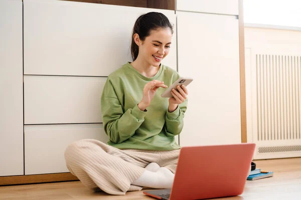 Lächelnde Junge Brünette Frau Benutzt Handy Während Sie Mit Laptop — Stockfoto