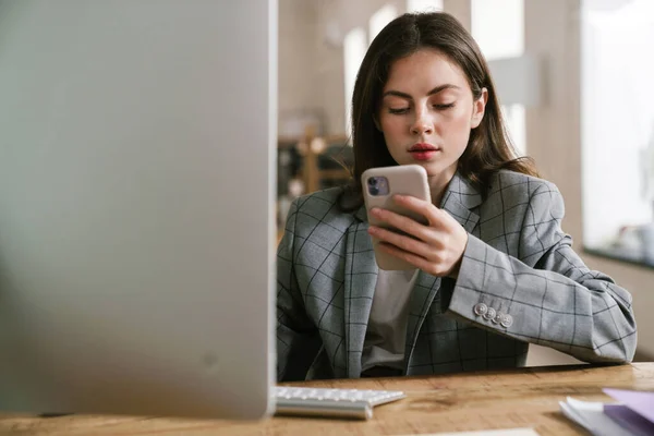 Jovem Morena Usando Telefone Celular Enquanto Trabalhava Com Computador Escritório — Fotografia de Stock