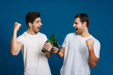 Heyecanlı yakışıklı adamlar ayı içiyor ve kazanan jestler yapıyor mavi arka planda izole edilmiş