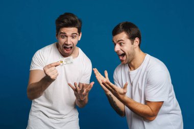 Excited two guys expressing surprise while posing with credit card isolated over blue background clipart
