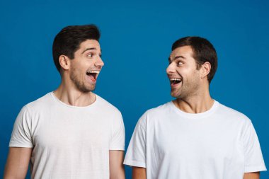 Heyecanlı, tıraşsız iki adam birbirlerine mavi arka planda izole bir şekilde bakarken bağırıyor.