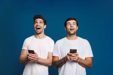 Mavi arka planda izole edilmiş akıllı telefonlarla poz veren iki adamı memnun ettim.