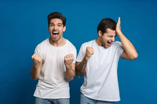 Podekscytowany Dwóch Facetów Krzyczy Podczas Dokonywania Gestu Zwycięzcy Izolowane Niebieskim — Zdjęcie stockowe