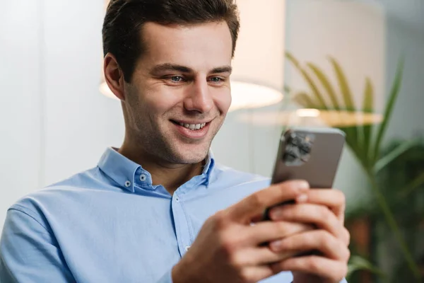 Sorrindo Bonito Jovem Empreendedor Usando Telefone Celular Enquanto Sentado Escritório — Fotografia de Stock