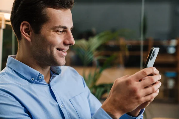 Sorrindo Bonito Jovem Empreendedor Usando Telefone Celular Enquanto Sentado Escritório — Fotografia de Stock