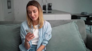 Odadaki koltukta otururken telefona bakan gülen kadın.