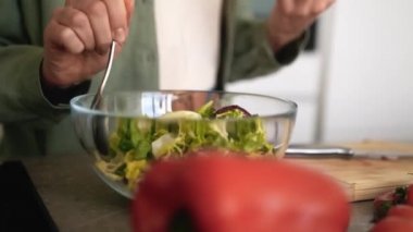 Kadın ellerinin şeffaf bir tabakta salata karıştırdığı yakın çekim görüntüsü.