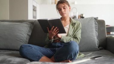 Odadaki kanepede oturmuş kitap okuyan pozitif bir kadın.