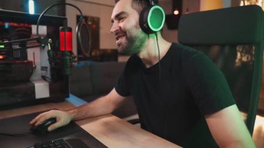 Kulaklık takan mutlu bir oyuncu evde oturan mikrofonla konuşurken profesyonel güçlü bir bilgisayardan çevrimiçi video oyunları izliyor.