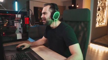 Kulaklık takan hoşnutsuz bir erkek oyuncu evde oturan güçlü profesyonel bilgisayardan çevrimiçi video oyunları izliyor.