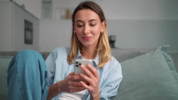 Mujer Feliz Hojeando Cinta Teléfono Mientras Está Sentada Sofá Habitación — Vídeo de stock