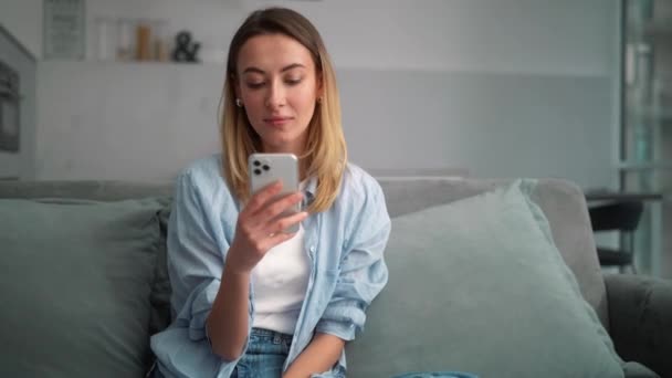 Mulher Positiva Digitando Algo Telefone Enquanto Senta Sofá Sala — Vídeo de Stock