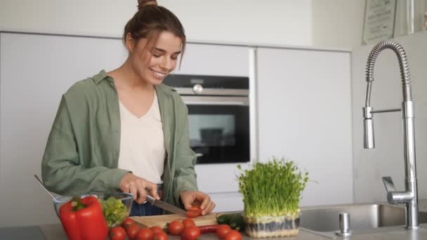 キッチンに立っている間にサラダ用のトマトを切る笑顔の女性 — ストック動画