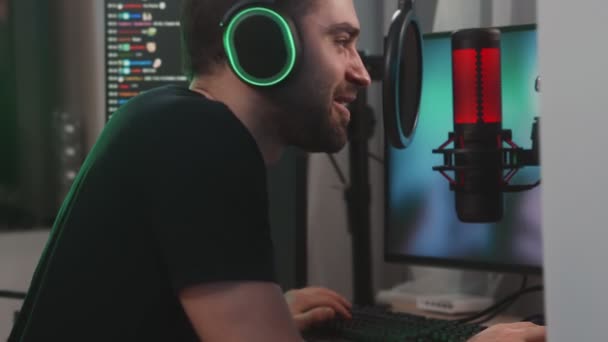 緑の画面が表示され プロの強力なコンピュータ上でオンラインビデオゲームをストリーミング幸せな男のゲーマーの側面図は 自宅に座ってマイクに話をしながら — ストック動画