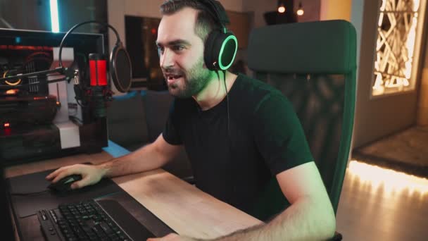 イヤフォンを身に着けている勝者の男のゲーマーは自宅に座ってプロの強力なコンピュータ上でオンラインビデオゲームをストリーミングしています — ストック動画
