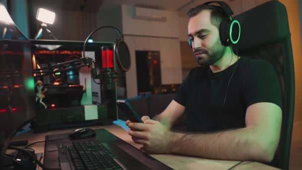 Hombre Sonriente Jugador Está Utilizando Teléfono Inteligente Mientras Está Sentado — Vídeos de Stock