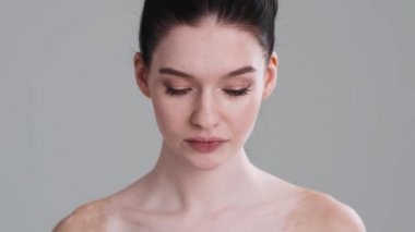 Vitiligo 'lu güzel yarı çıplak bir kadın stüdyodaki gri duvarın üzerinde yalnız başına kameraya poz veriyor. Çeşitlilik toleransı. Herkes çok güzel.