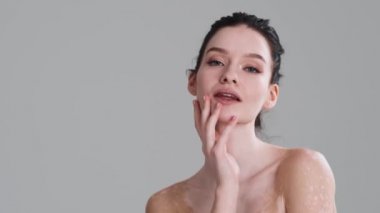 Yakışıklı yarı çıplak bir kadın, stüdyodaki gri duvarın üzerinde kameraya poz verirken boynuna dokunuyor. Çeşitlilik toleransı. Herkes çok güzel.