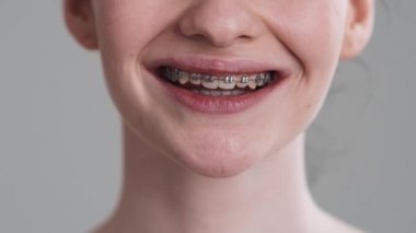 Kameraya gülümseyen bir kadının yakın çekim görüntüsü stüdyodaki gri duvarın üzerinde izole bir şekilde duruyor.