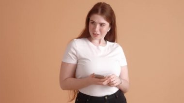 Pozitif ve iri yarı kızıl saçlı bir kadın stüdyodaki bej bir duvarın üzerinde dans ediyor.