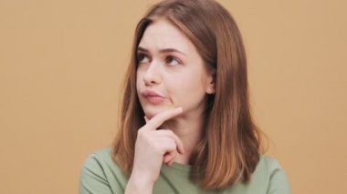 Ciddi bir genç kadın stüdyodaki bej bir duvarın arkasında duran bir şeyi düşünüyor.