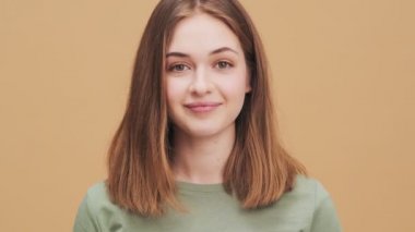 Pozitif bir genç kadın stüdyodaki bej bir duvarın arkasında durmuş selam veriyor.