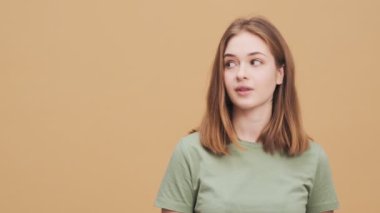 Gülümseyen genç bir kadın, stüdyodaki bej bir duvarın üzerinde duran yan tarafı işaret ediyor.