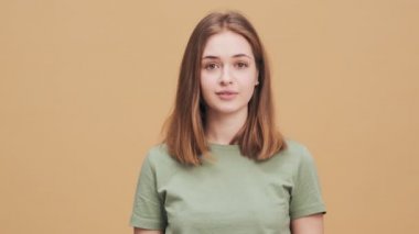 Mutlu genç bir kadın, stüdyodaki bej bir duvarın üzerinde ellerini çırparken kameraya bakıyor.