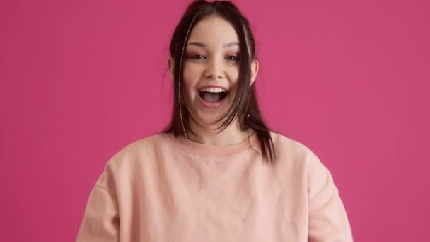一个快乐的少女在工作室里孤零零地站在粉红的墙壁上做着获胜的手势 — 图库视频影像