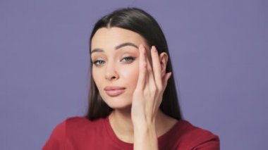 Çekici genç bir kadının kırpılmış görüntüsü, stüdyodaki mor bir arka planda tek başına duran aynaya bakar gibi yüzüne bakıyor.