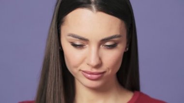 Ciddi bir genç kadının yakın plan görüntüsü stüdyodaki mor bir arka planda tek başına kameraya bakıyor.