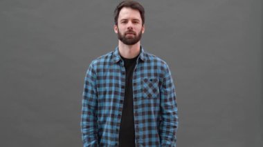 Ekose gömlekli gülümseyen adam gri bir stüdyoda hoş bir jest gösteriyor.