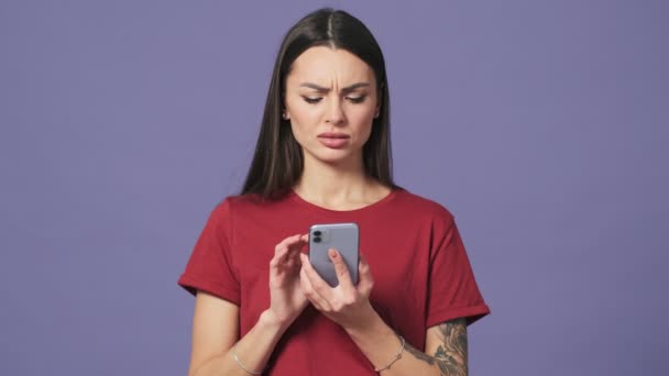 一位愤怒的年轻女子用她的智能手机站在工作室的紫色背景上 与外界隔绝 — 图库视频影像
