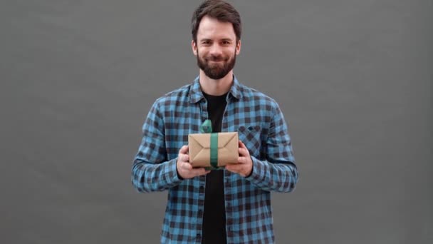 Šťastný Muž Kostkované Košili Drží Dárek Kameře Zatímco Stojí Šedém — Stock video