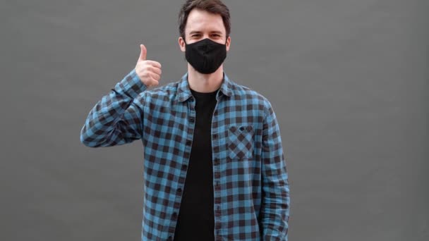 Hombre Sonriente Con Una Máscara Protectora Negra Mostrando Gesto Pulgar — Vídeos de Stock