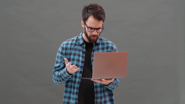 这位愤愤不平的戴眼镜的男人没有在笔记本电脑里找到什么东西 而是站在一间灰色的工作室里 手里拿着它 — 图库视频影像