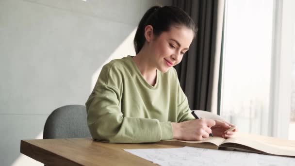 Pozytywna Kobieta Pisząca Coś Papierze Siedząc Pokoju Przy Oknie — Wideo stockowe