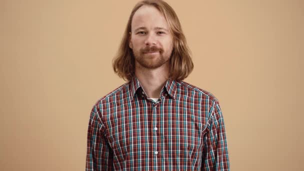ベージュのスタジオに立っている間 負の彼の頭を振る再生シャツの長い髪を持つ男 — ストック動画