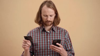 Ekose gömlekli, uzun saçlı bir adam bej renkli bir stüdyoda dururken telefona banka kartı numarası yazıyor.