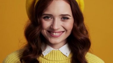 Sarı stüdyoda dururken gülümseyen bir kadının yanaklarına dokunuşunun yakın plan görüntüsü.